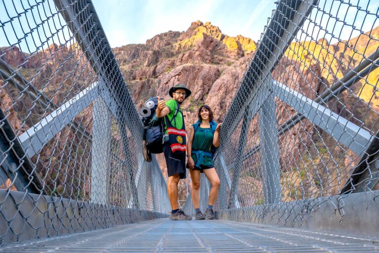 A couple hiking in the Grand Canyon stops for a photo on a bridge